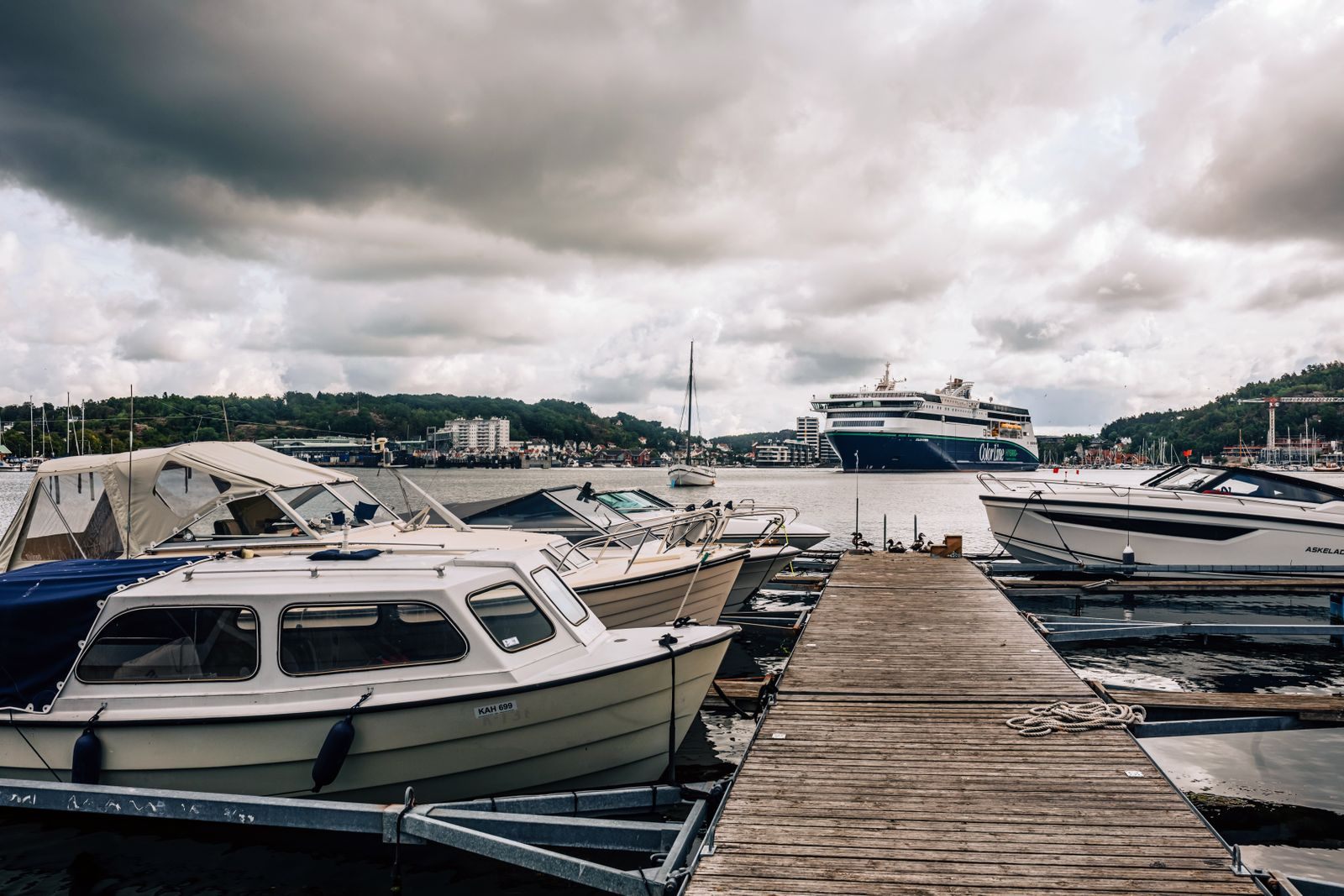 Small boats at a wooden jetty with a cruise ship in the harbour under heavy clouds