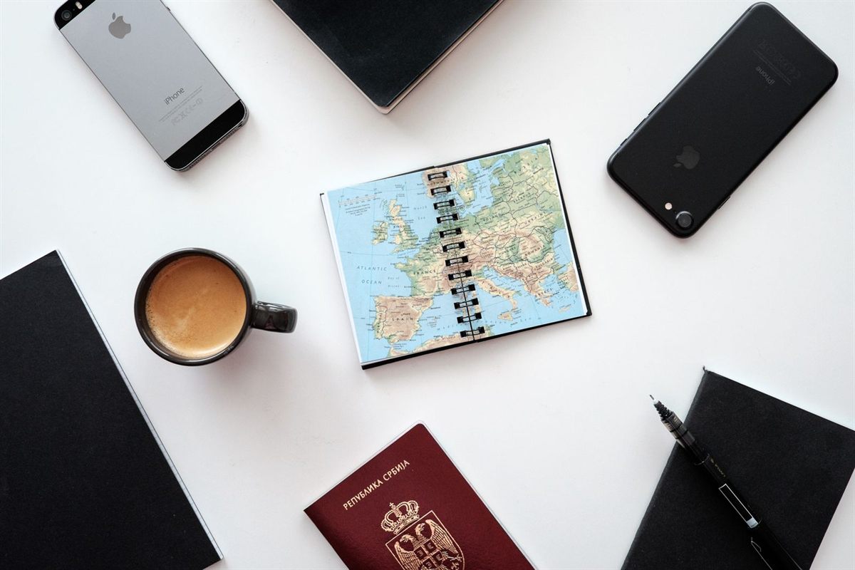A passport, a map notebook, coffee and phones laid out on a white table