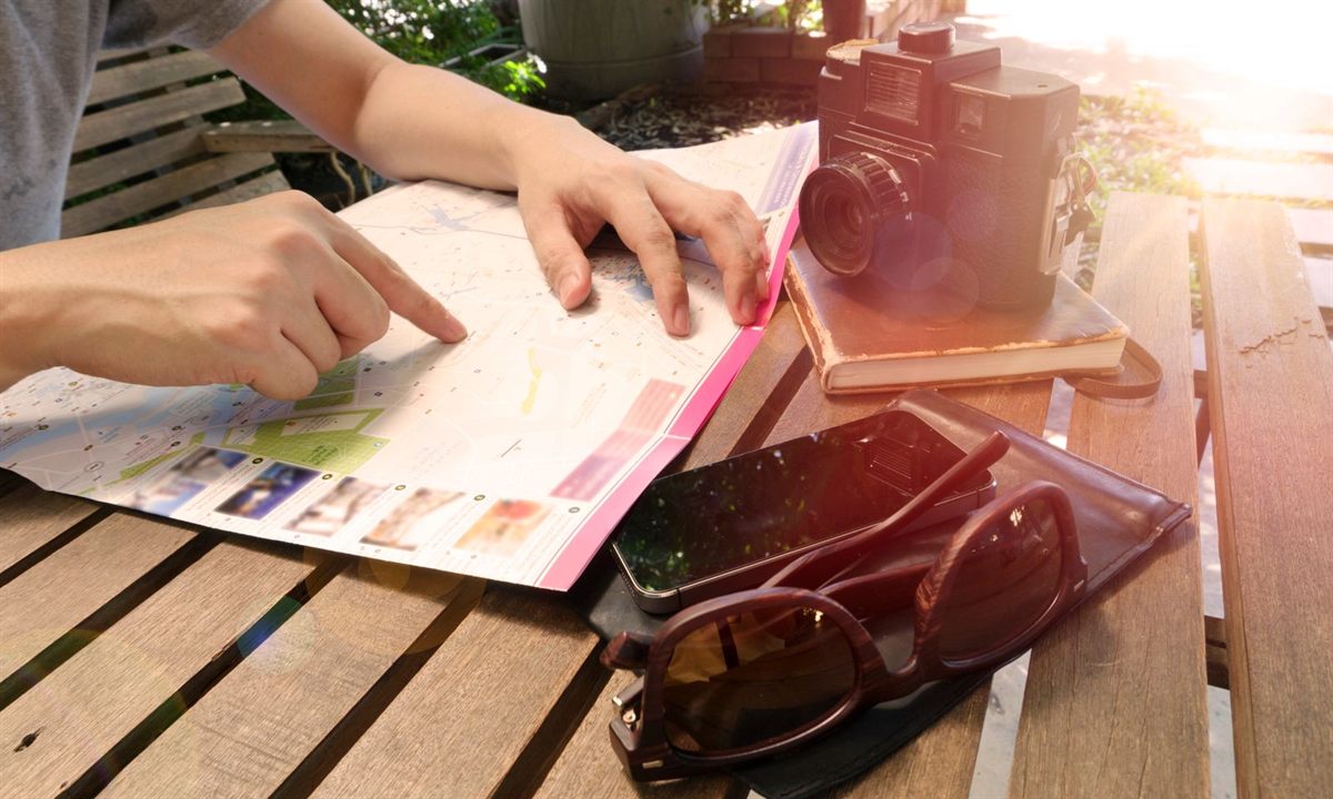 A traveller pointing at a paper map on a wooden table next to a camera