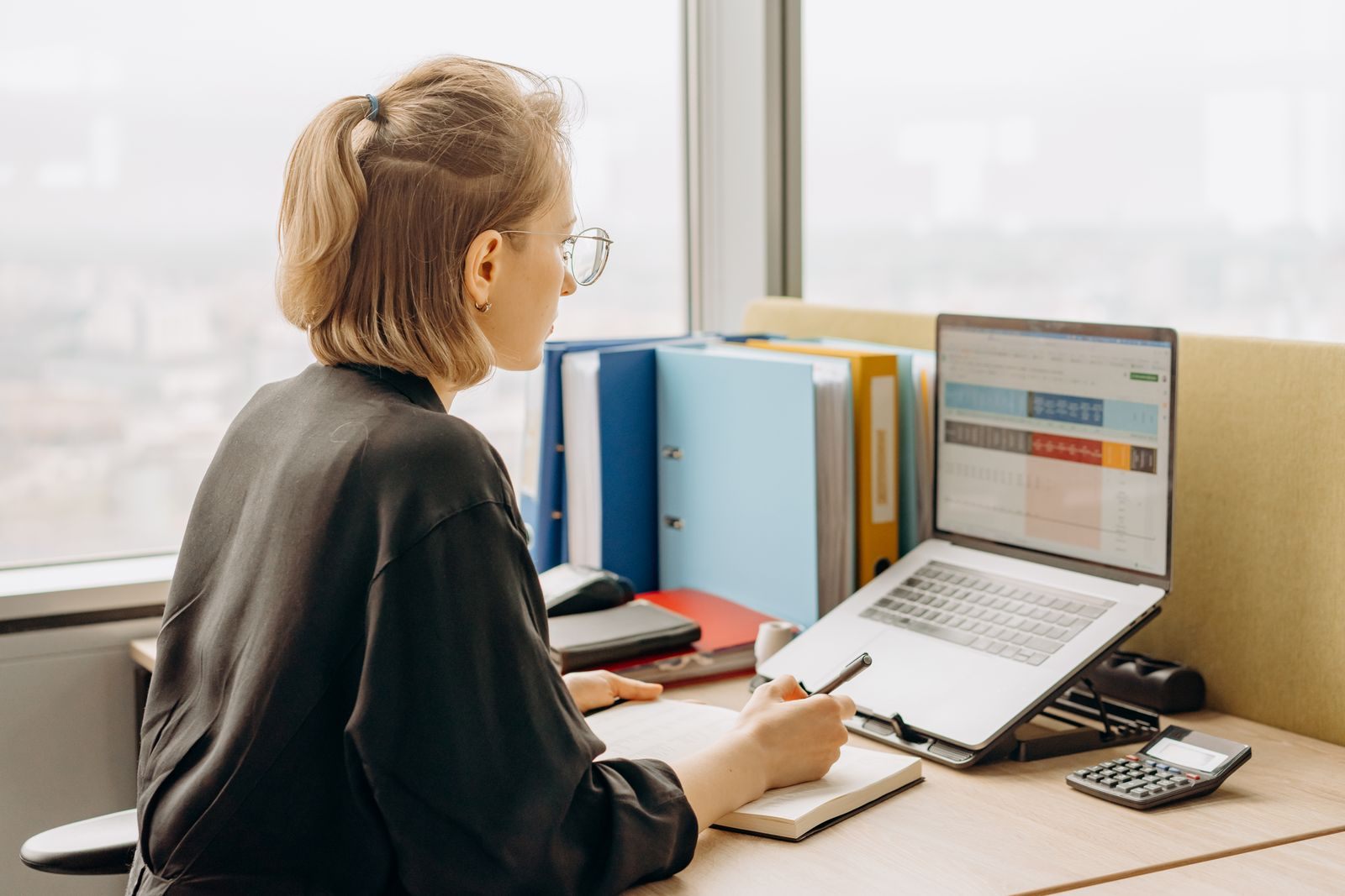 A woman working at a laptop with folders and a calculator, filling in a cruise planning spreadsheet