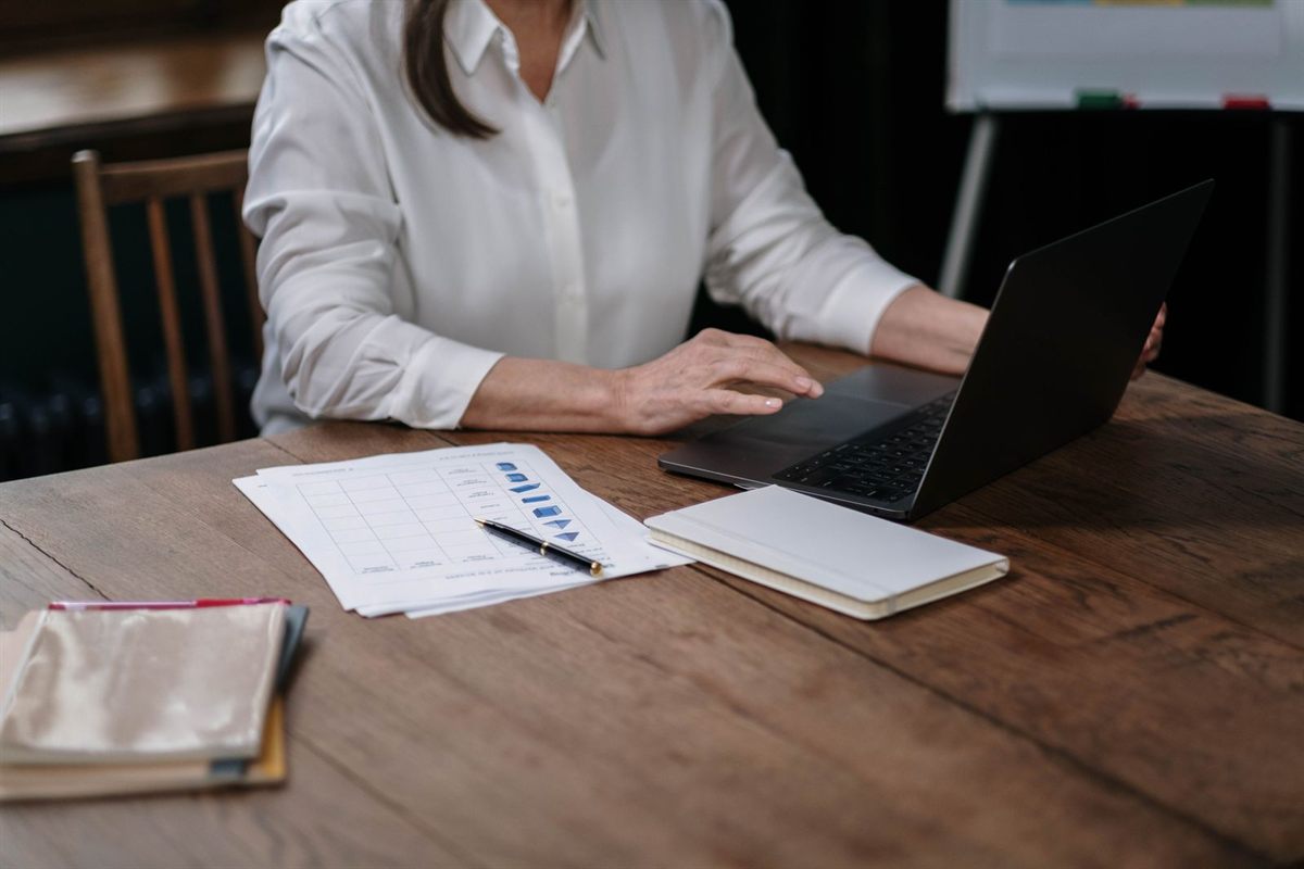 A woman typing on a laptop at a wooden desk with papers beside her