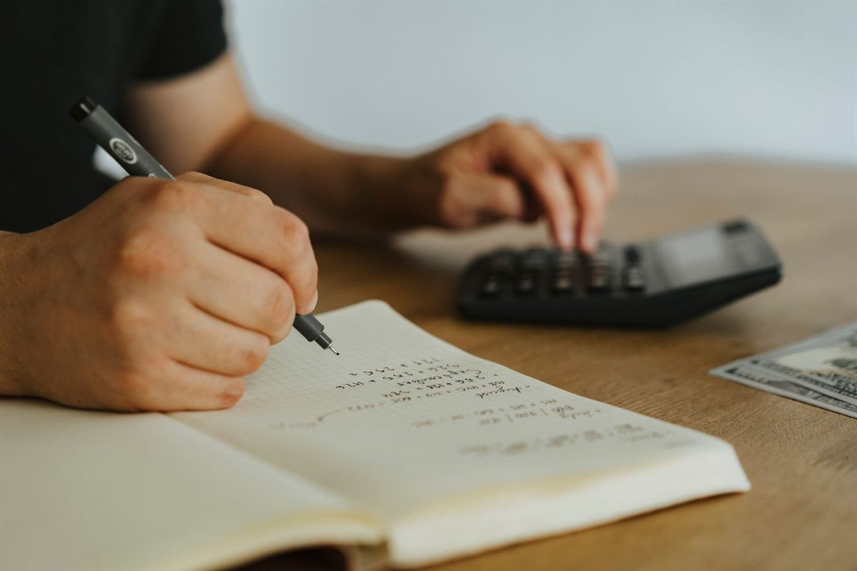 Hands writing calculations in a notebook next to a calculator